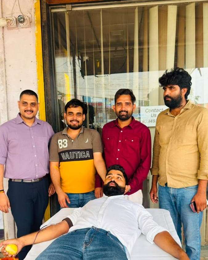 Blood donor squeezing a ball while volunteers stand beside him at the Allomart Pharmacy camp on Sikar Road, Jaipur